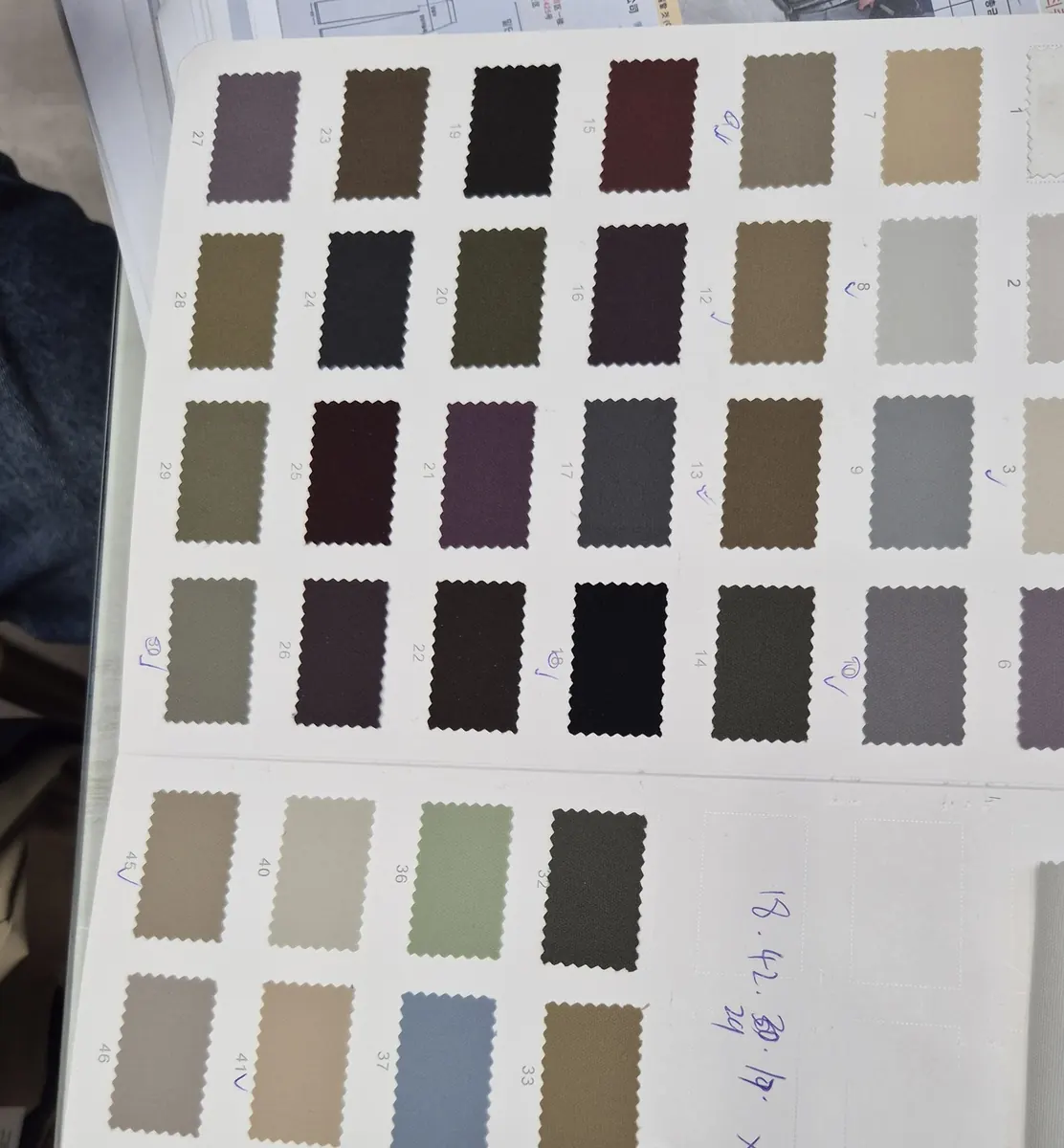 A mill's colour card of fabric swatches on a desk, with shortlisted numbers marked by hand