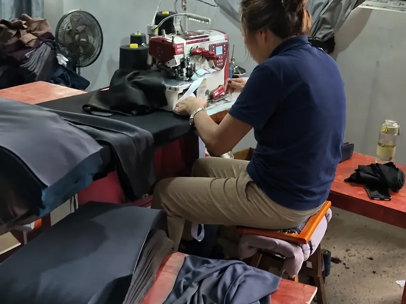 An operator working at a sewing station with cut panels stacked beside her