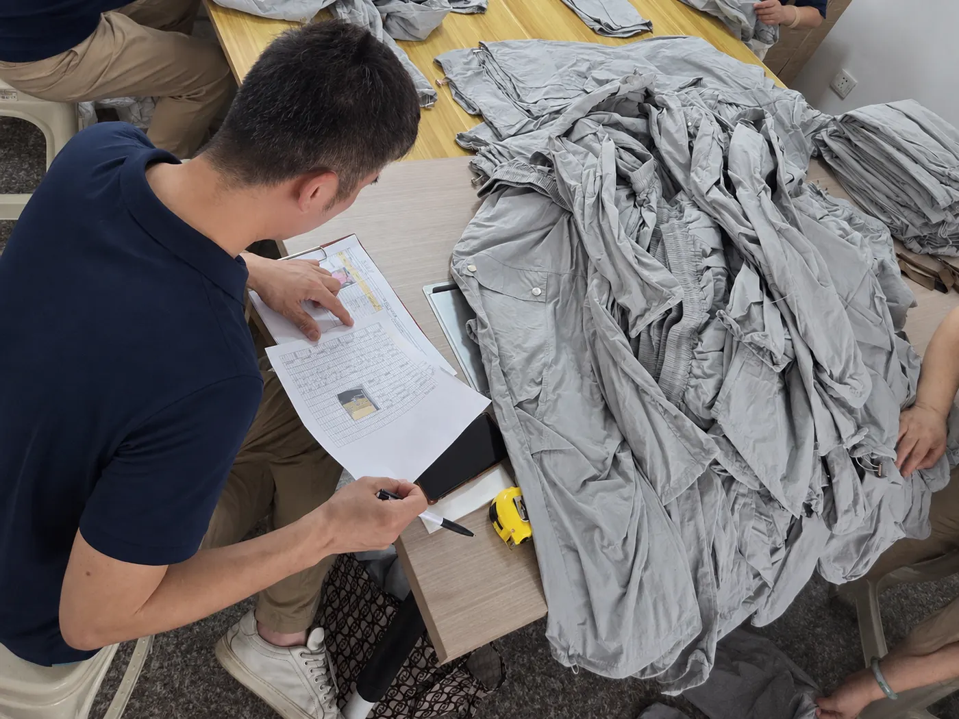 Our staff recording results on a QC checksheet with a tape measure while the team inspects finished garments